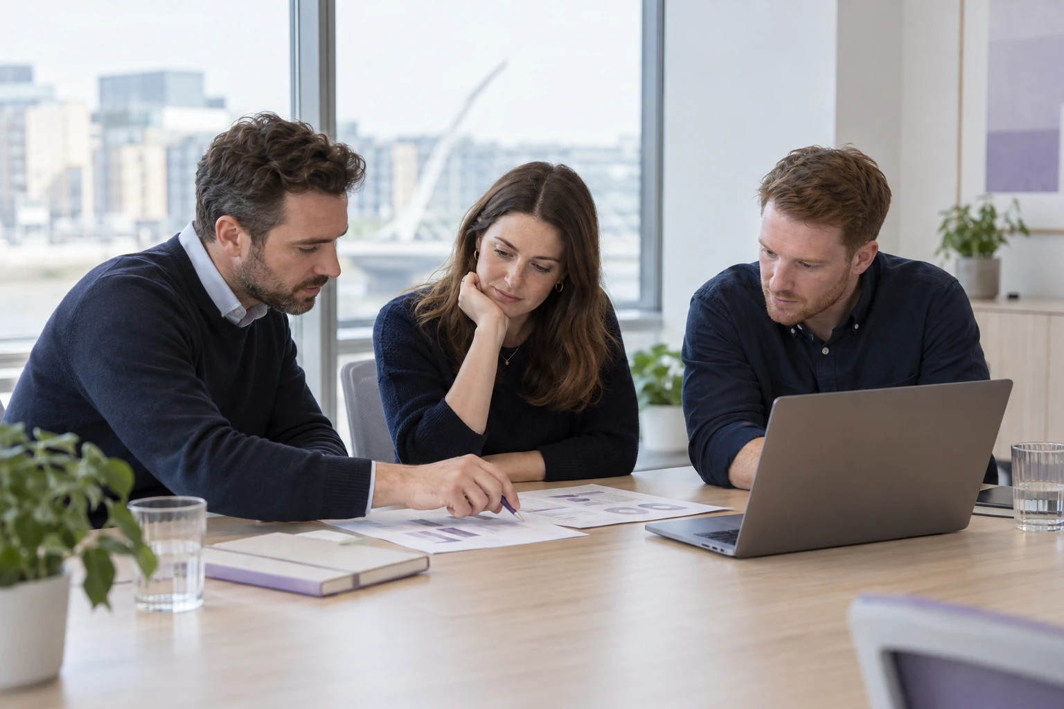 Three consultants reviewing printed data planning documents and a laptop around an office table.